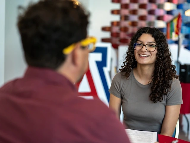 A University of Arizona employee smiles while speaking with a colleague during a one-on-one meeting. The colleague is seated in the foreground with their back to the camera, while university-themed decorations are visible in the background.