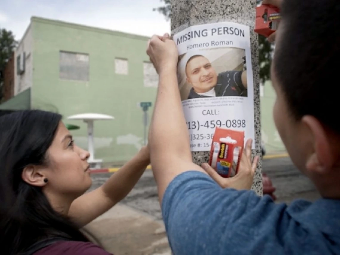 two people hanging up a sign for a missing person