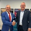 Two men shake hands in front of several engineering posters